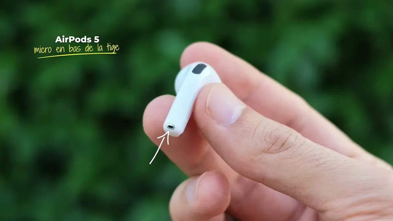 Un écouteur AirPods 5 tenu entre deux doigts, une flèche montre le micro au bout de la tige