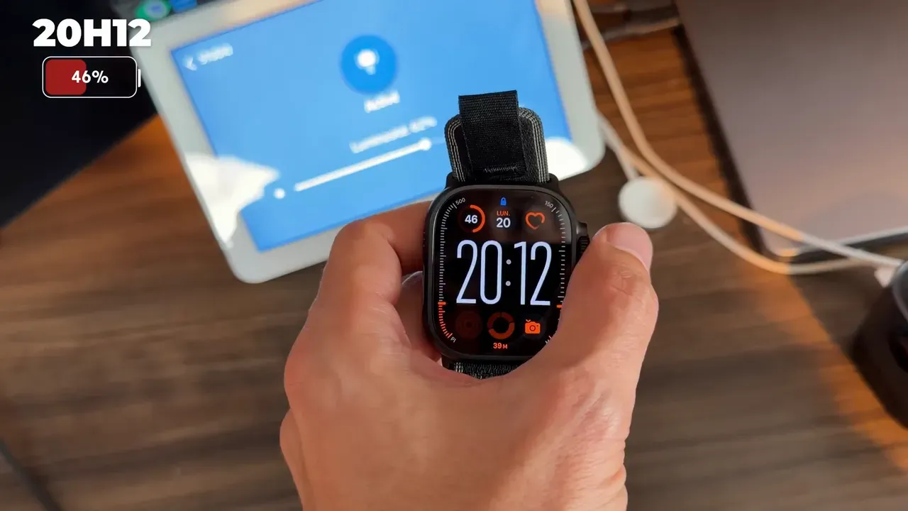 L’Apple Watch Ultra 3 en main à côté de son chargeur, à 46 % de batterie