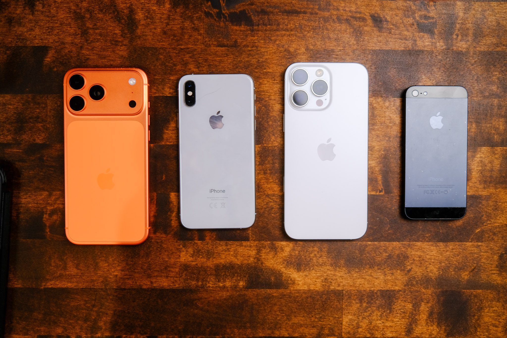 Quatre iPhone de générations différentes posés à plat côte à côte sur une table en bois, vus de dos