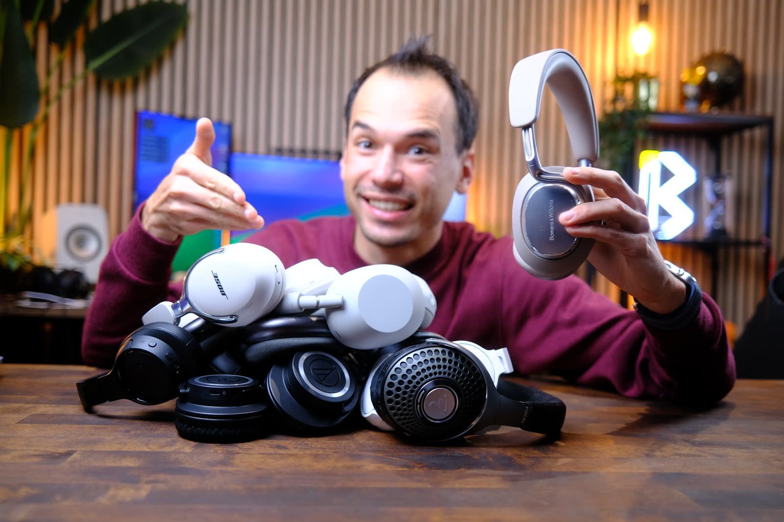 Kévin au studio, lattes de bois et écrans derrière lui, montre du doigt une pile de casques posée devant lui sur le bureau