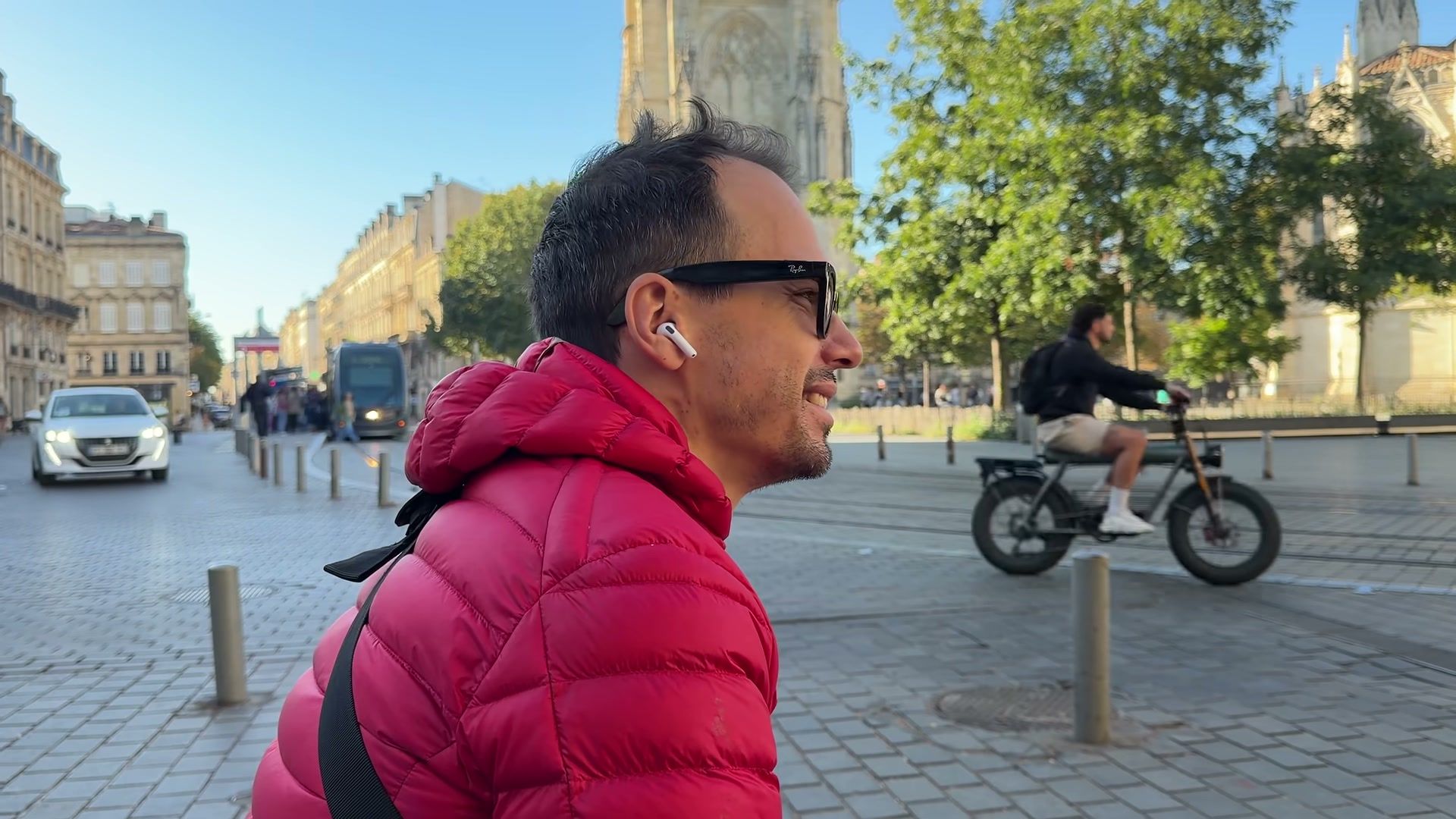Kévin porte les AirPods 5 en ville, sur une place pavée