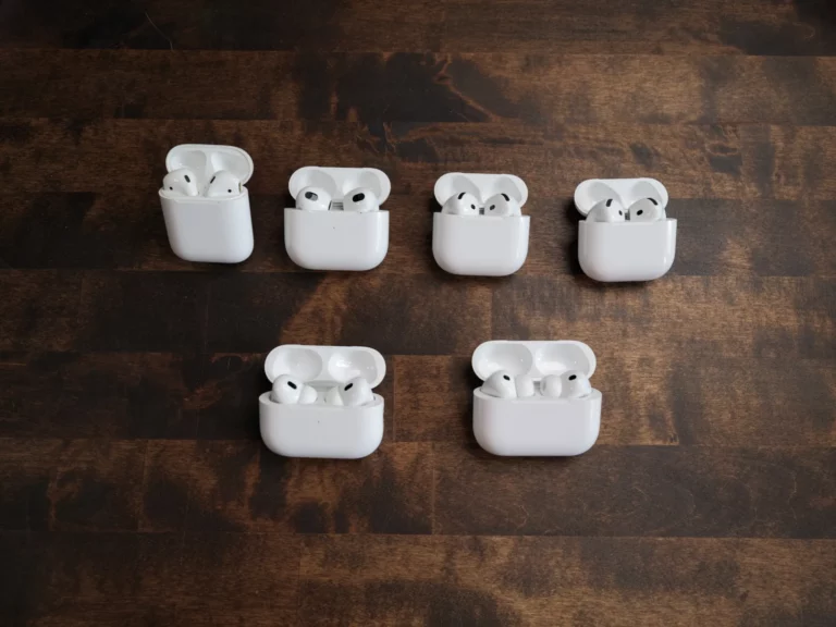 Six boîtiers d'AirPods ouverts sur une table en bois : AirPods 2, 3, 4, 5, Pro 2 et Pro 3